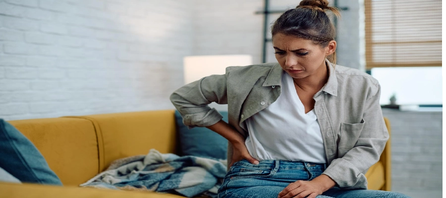 mulher sentada no sofá com sintomas de infecção nos rins