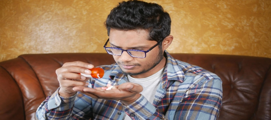 Imagem do post homem sentado no sofá com comprimidos na mão