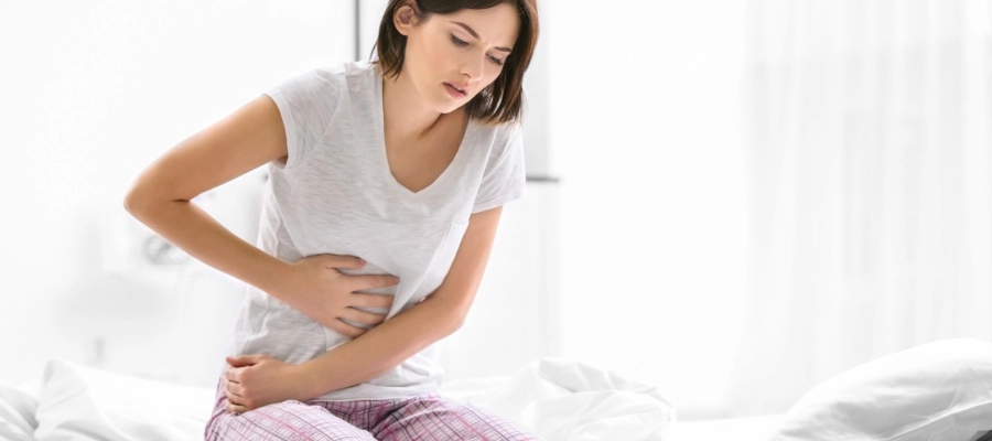Imagem do post uma mulher sentada em uma cama com dor no estômago