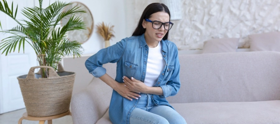 uma mulher sentada em um sofá com dor na lateral do abdômen