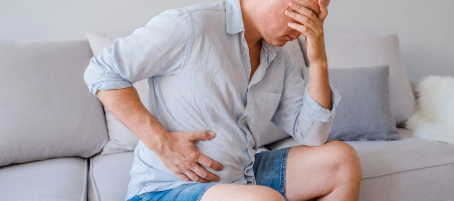 Imagem do post homem apoia a cabeça nas mãos e segura a lateral da barriga