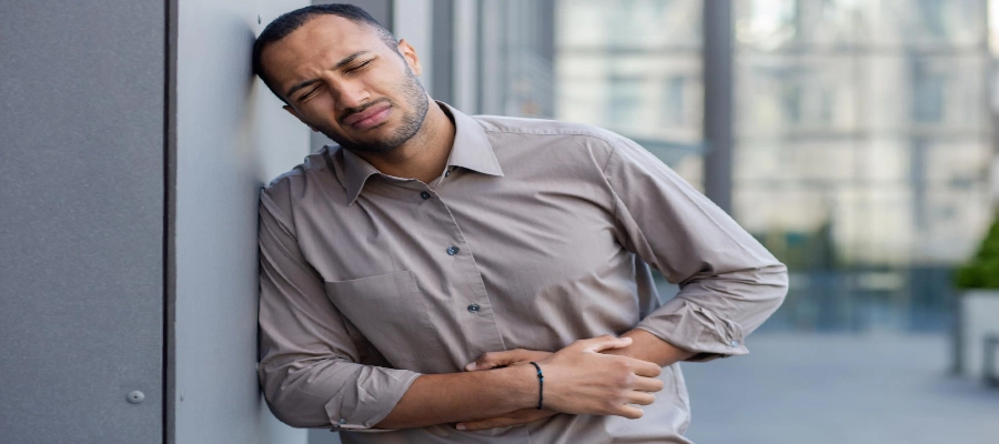 Imagem do post Homem encostado em uma parede com expressão de dor, segurando o abdômen, indicando dor na barriga ou desconforto gastrointestinal.