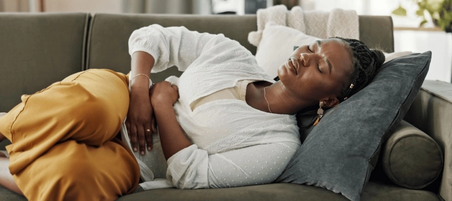 Imagem do post mulher deitada no sofá com dor busca tratamento para pedra na vesícula