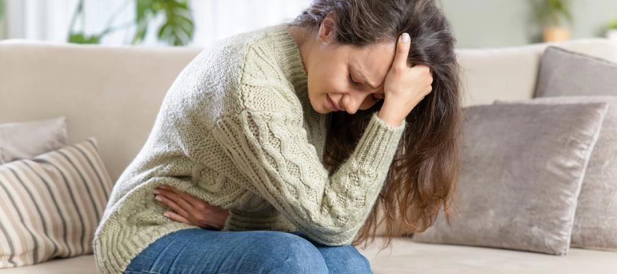 Imagem do post uma mulher sentada no sofá se contorce com dor abdominal