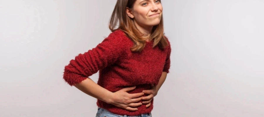 Mulher com as mãos na barriga, com expressão de dor de estômago, forte desconforto abdominal