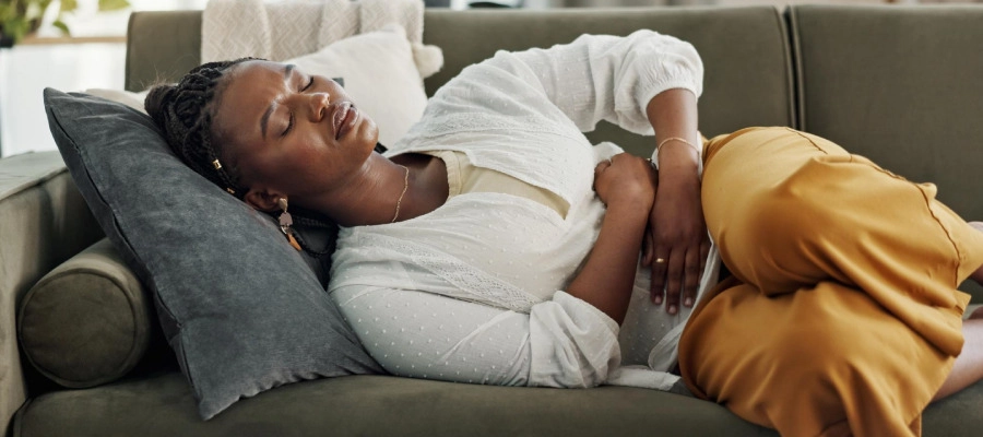 Imagem do post mulher negra deitada no sofá com cólica