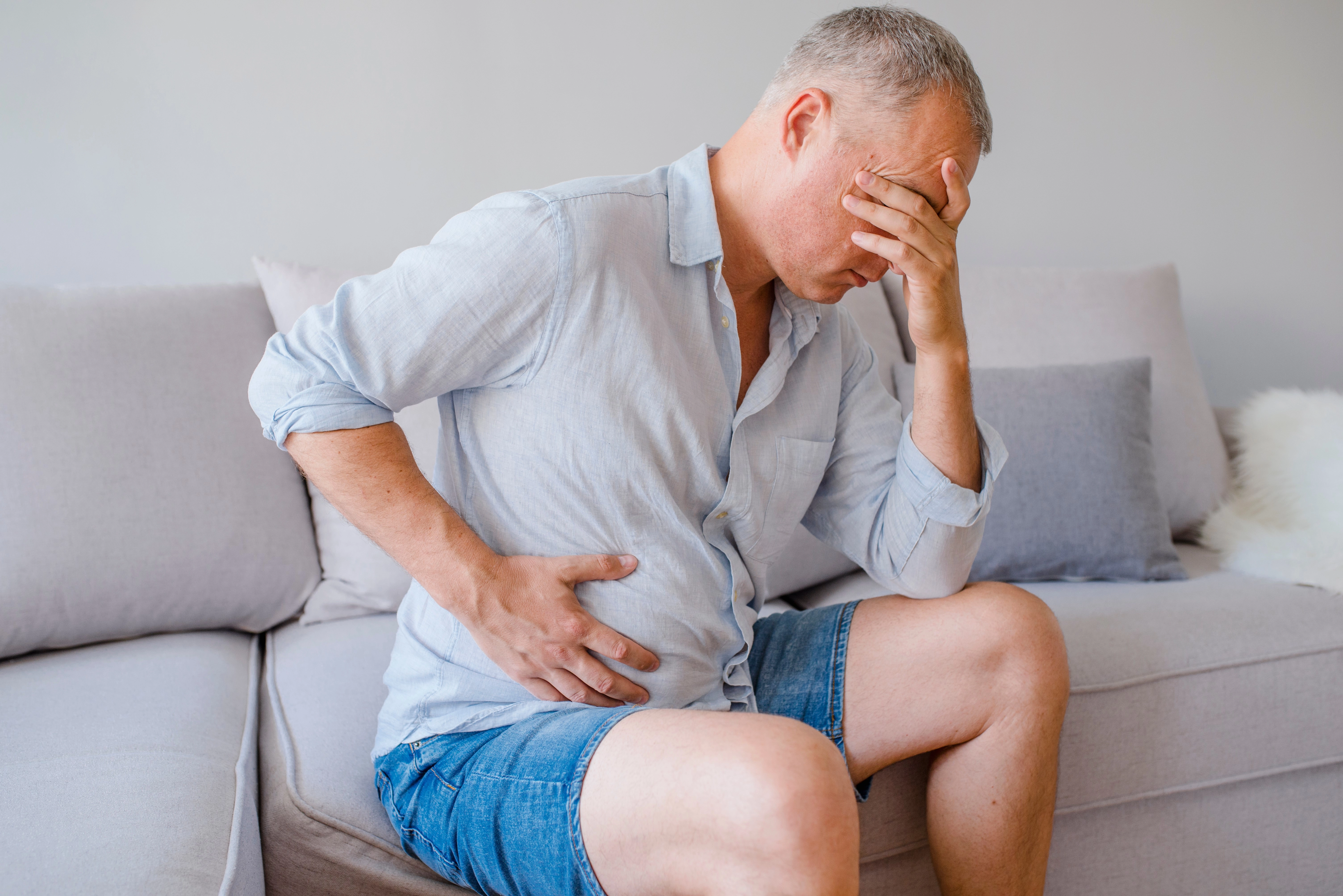 Imagem do post um homem sentado em um sofá com a mão na lateral da barriga