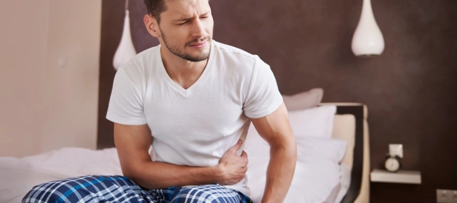 Imagem do post um homem sentado em uma cama com a mão na barriga
