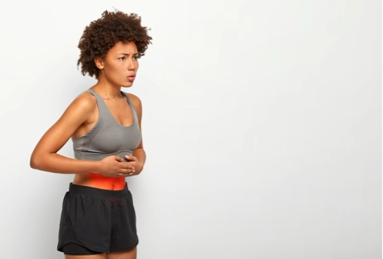 Imagem do post uma mulher em um top cinza e shorts pretos segura a barriga