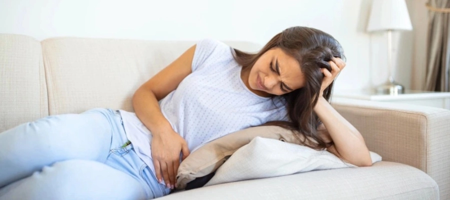 Imagem do post uma menina sentada em sua cama com dor no estômago