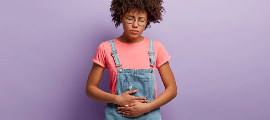 Imagem do post uma menina de macacão e óculos de pé contra uma parede roxa
