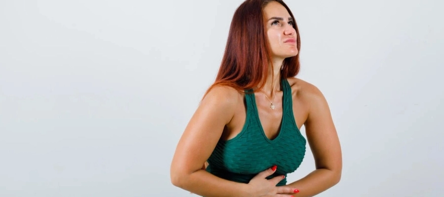 Imagem do post mulher com cabelos compridos com as mãos na barriga sentindo desconforto.