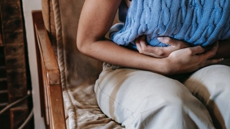 Imagem do post uma mulher sentada em um sofá com um suéter azul e mão na barriga