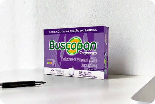 Embalagem do produto Buscopan Composto em cima de uma mesa, ao lado de uma caneta.