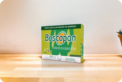 Embalagem do produto Buscopan em cima de um piso de madeira.